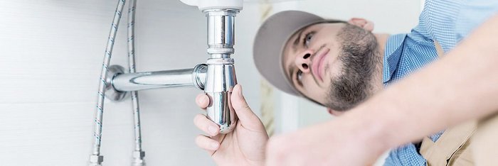 Ein Handwerker überprüft sorgfältig die Rohrverbindungen unter einem Waschbecken, um sicherzustellen, dass alles dicht ist.